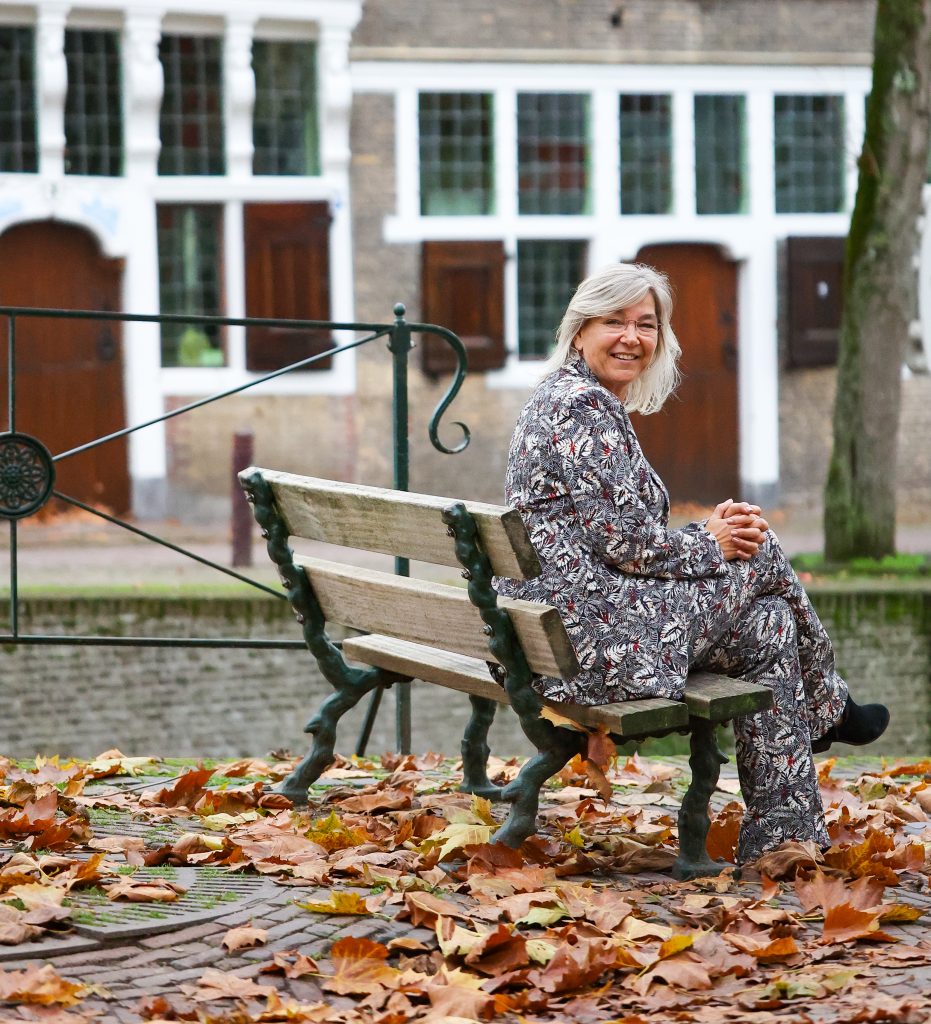 Melanie van De MEL Methode zit ontspannen op een bankje in een rustige buitenomgeving.
